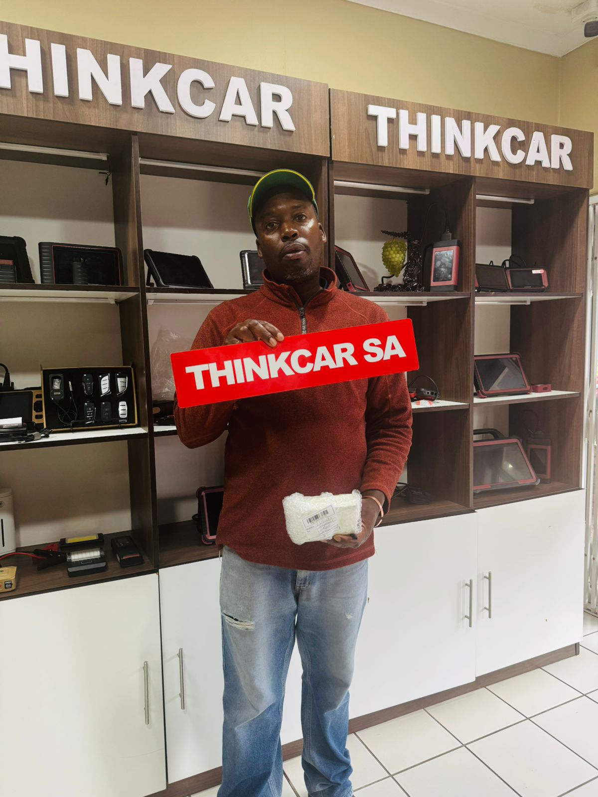 happy client - Launch SA Man in a red sweater holding a red THINKCAR SA sign inside a ThinkCar store.